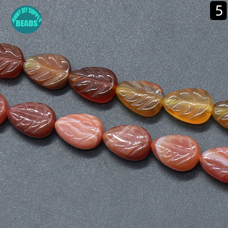 May include: A strand of orange and pink gemstone beads with a leaf design. The beads are strung on a clear thread and are approximately 1 cm in diameter.