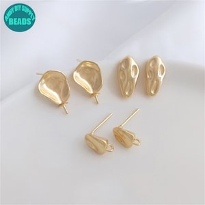 May include: Five gold-toned earring findings. Two are oval shaped with a textured surface. Two are irregular shaped with a smooth surface. One is a hook-shaped finding with a loop at the end.