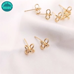 May include: Gold-toned butterfly shaped earring findings. The findings have a post and a butterfly shaped loop. The findings are on a white surface.