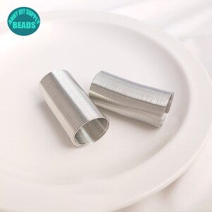 May include: Two coils of silver-colored wire, each coiled into a cylinder shape, are displayed on a white plate. The coils are made of thin wire and are approximately 2 inches in diameter.