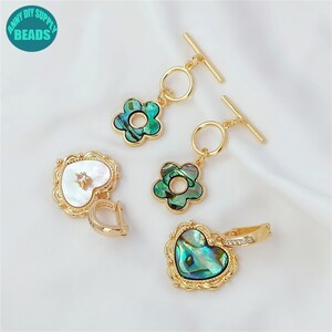 May include: Two pairs of gold-tone earrings with a heart and flower design. The heart earrings feature a white shell with a rhinestone in the center. The flower earrings feature a green and blue shell with a gold ring in the center.