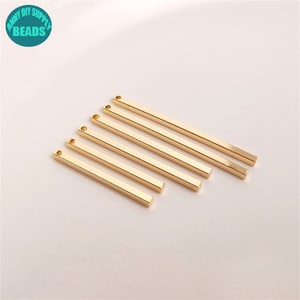 Peut inclure: Six pendentifs en forme de barre en métal de couleur dorée avec une petite boucle en haut. Les barres sont rectangulaires et ont une finition lisse et polie.