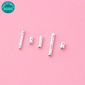 May include: Five silver metal spacer beads with a textured diamond pattern. The beads are arranged in a row on a pink background.