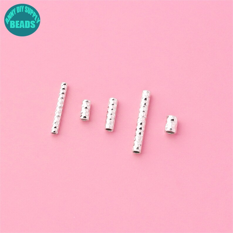 May include: Five silver metal spacer beads with a textured diamond pattern. The beads are arranged in a row on a pink background.