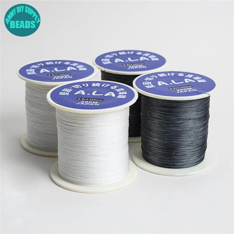 Puede incluir: Tres carretes de hilo blanco, gris y negro. Cada carrete est&aacute; etiquetado con el texto "A.LA 2.6-0.265mm 200M JAP&Oacute;N".