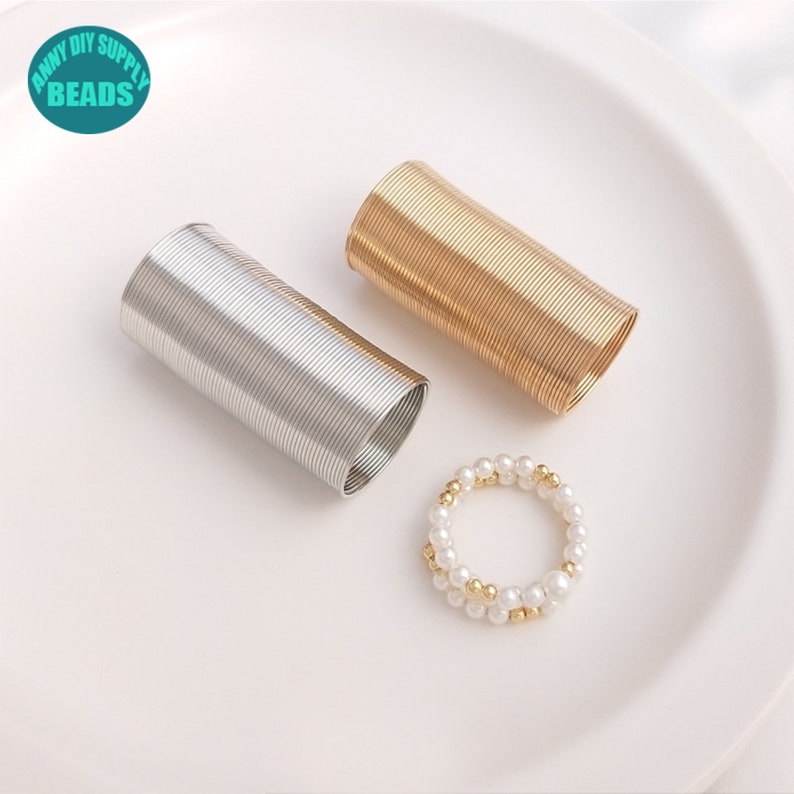 May include: Two spools of wire, one gold and one silver, and a pearl and gold bead ring. The spools are coiled and ready to be used for jewelry making.
