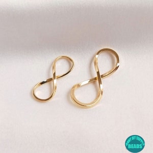 Könnte beinhalten: Zwei goldene Unendlichkeits-Anhänger, einer größer als der andere, auf weißem Hintergrund.