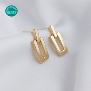 May include: A pair of gold-toned earrings with a simple, geometric design. Each earring features two linked rectangular shapes.
