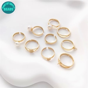 May include: A set of ten gold-toned adjustable ring bases with different styles, including some with a round bezel and some with a pearl accent.  The ring bases are perfect for creating custom jewellery.