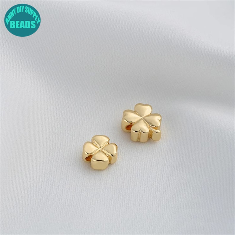 Op de afbeelding: Twee goudkleurige klavertjesvier-charms. De charms zijn gemaakt van metaal en hebben een glanzende afwerking. Ze zijn perfect om een ​​tikje geluk toe te voegen aan sieraden of knutselwerk.