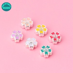 Op de afbeelding: Zes zilveren bloemencharms met verschillende gekleurde emaille centra. De kleuren zijn roze, geel, wit, rood, groen en perzik.