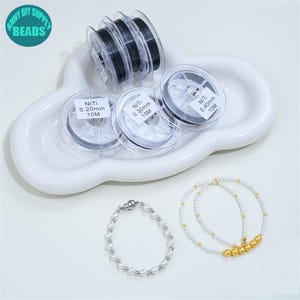 Puede incluir: Tres bobinas de plástico transparente con hilo NiTi negro etiquetadas de 0,20 mm, 0,30 mm y 0,40 mm en longitudes de 10 m, junto a dos pulseras de cuentas. Una pulsera tiene perlas blancas con detalles plateados y la otra perlas blancas y doradas.