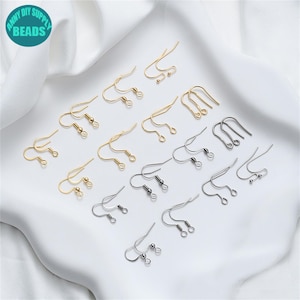 Könnte beinhalten: Eine Auswahl an gold- und silberfarbenen Ohrringhaken. Das Bild zeigt verschiedene Arten von Haken, darunter französische Haken und Fischhaken. Der Text "ANNY DIY SUPPLY BEADS" ist in einem kreisförmigen Logo zu sehen.