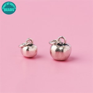 May include: Two silver apple charms with a loop for attaching to a necklace or bracelet. The charms are different sizes.