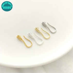 May include: Four metal earring hooks, two in a gold tone and two in a silver tone, each featuring a textured, tulip-shaped decorative element at the top. The hooks are arranged in a row, showcasing a curved, elongated design for jewelry making.