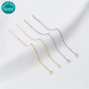 May include: Three pairs of threader earrings in gold and silver. Each earring has a straight post and a fine chain ending in a small loop. The earrings are shown on a white surface. The image includes a teal circle with the text "ANNY DIY SUPPLY BEADS".