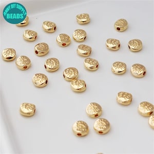 May include: A collection of gold-coloured metal beads with an eye design. The beads are scattered on a white surface.