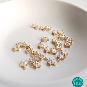 Puede incluir: Una colecci&oacute;n de abalorios en forma de estrella de color dorado con detalles de cristal transparente. Los abalorios tienen un bucle en la parte superior para sujetarlos a joyas u otras manualidades.