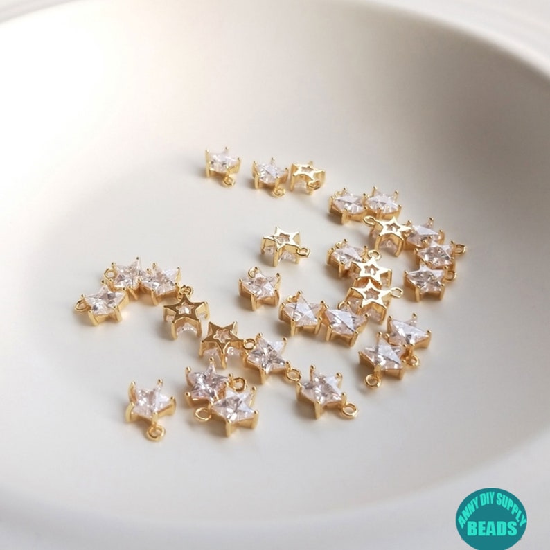 Puede incluir: Una colecci&oacute;n de abalorios en forma de estrella de color dorado con detalles de cristal transparente. Los abalorios tienen un bucle en la parte superior para sujetarlos a joyas u otras manualidades.