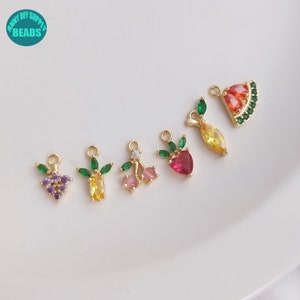 Può includere: Sei ciondoli di frutta colorati con foglie verdi e dettagli dorati. I ciondoli sono in metallo e presentano vari frutti, tra cui un'anguria, un ananas, una ciliegia, una fragola, un'uva e un limone.
