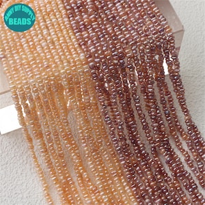 Può includere: Primo piano di più fili di piccole perline di forma irregolare nei toni del pesca, beige e marrone. Le perline sono infilate insieme, creando un effetto a cascata. L'immagine include un logo circolare che dice "ANNY DIY SUPPLY BEADS".