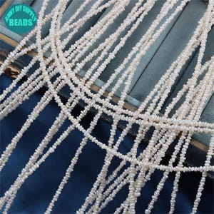 May include: Close-up of multiple strands of white, irregular-shaped beads. The beads are strung together, creating a delicate, textured appearance. The image includes the text "ANNY DIY SUPPLY BEADS" in a circular logo.
