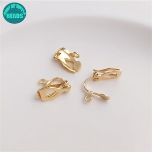 May include: Three gold-toned earring clips. The clips are designed to be worn on the earlobe and have a small loop at the top for attaching earrings.