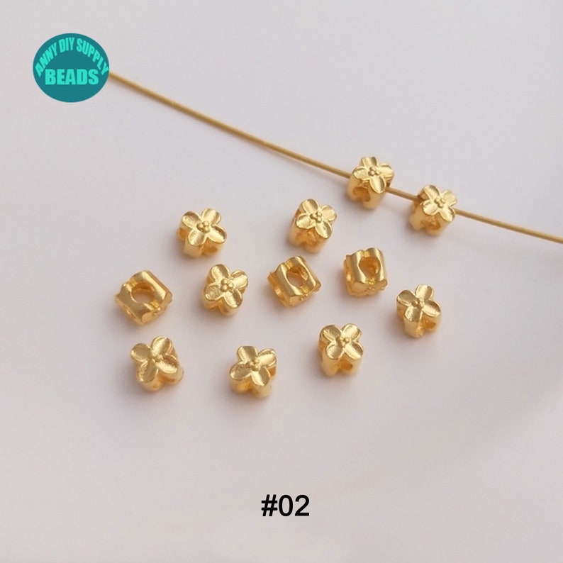 May include: Gold flower-shaped spacer beads with a square hole in the center. The beads are scattered on a white surface. #02