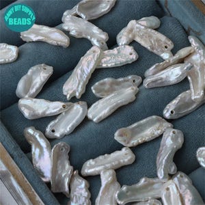 Può includere: Perline di perle barocche bianche iridescenti con fori, sparse su una superficie verde acqua. Le perline hanno forme irregolari e una finitura lucida, perfette per la creazione di gioielli. Il testo "ANNY DIY SUPPLY BEADS" è presente.