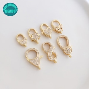 May include: A set of six gold-tone metal clasps with clear rhinestone embellishments. The clasps are in various shapes, including a star, heart, butterfly, infinity symbol, and two oval shapes.
