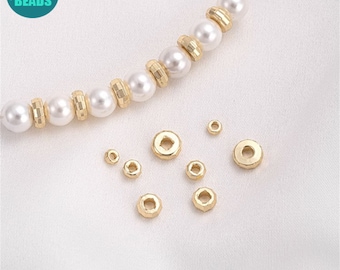 May include: A close-up of gold-colored metal spacer beads. The beads have a faceted design and a hole in the center. The beads are arranged in a scattered pattern on a white surface.