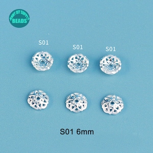 May include: Six silver-colored, open-work bead caps, each 6mm in diameter, are arranged on a light blue surface. The bead caps have a floral design. The text "S01" is above each bead cap. The text "S01 6mm" is at the bottom.