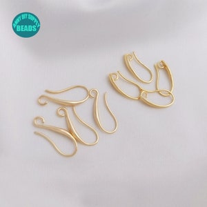 May include: A close-up of eight gold-toned earring hooks, also known as jump rings, on a white surface. The hooks are made of metal and have a smooth, polished finish.
