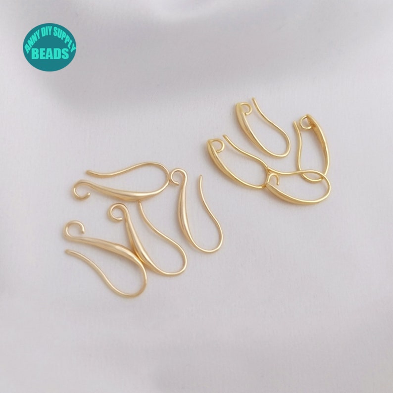 May include: A close-up of eight gold-toned earring hooks, also known as jump rings, on a white surface. The hooks are made of metal and have a smooth, polished finish.