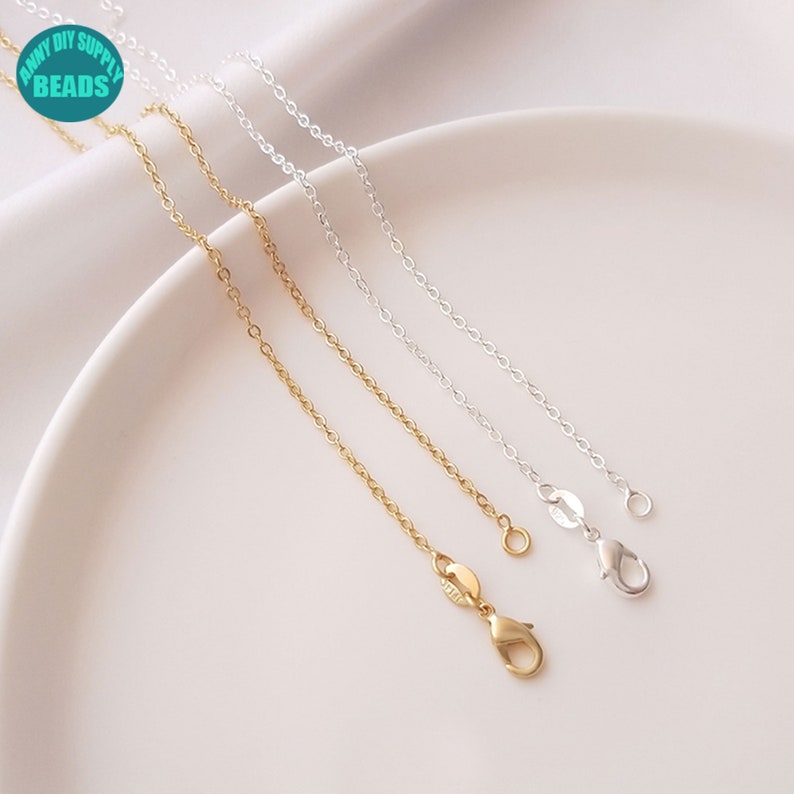 May include: Three silver chains with lobster clasps. The chains are on a white surface.