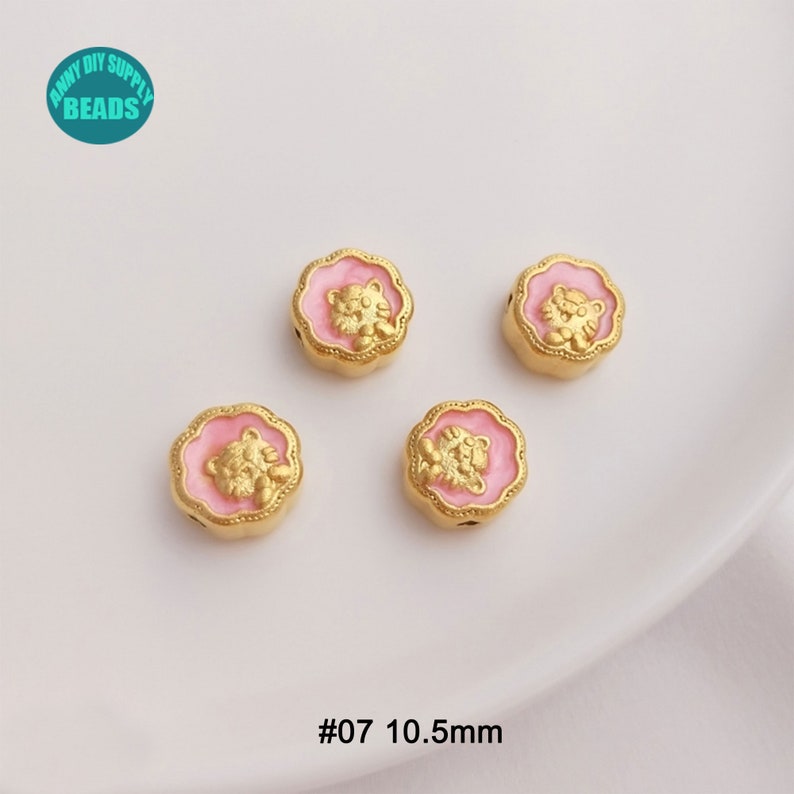 May include: Four gold-colored, round beads with a pink floral border and a gold tiger design. The beads are 10.5mm in diameter. The text "#07 10.5mm" is at the bottom. The beads are from ANNY DIY SUPPLY BEADS.