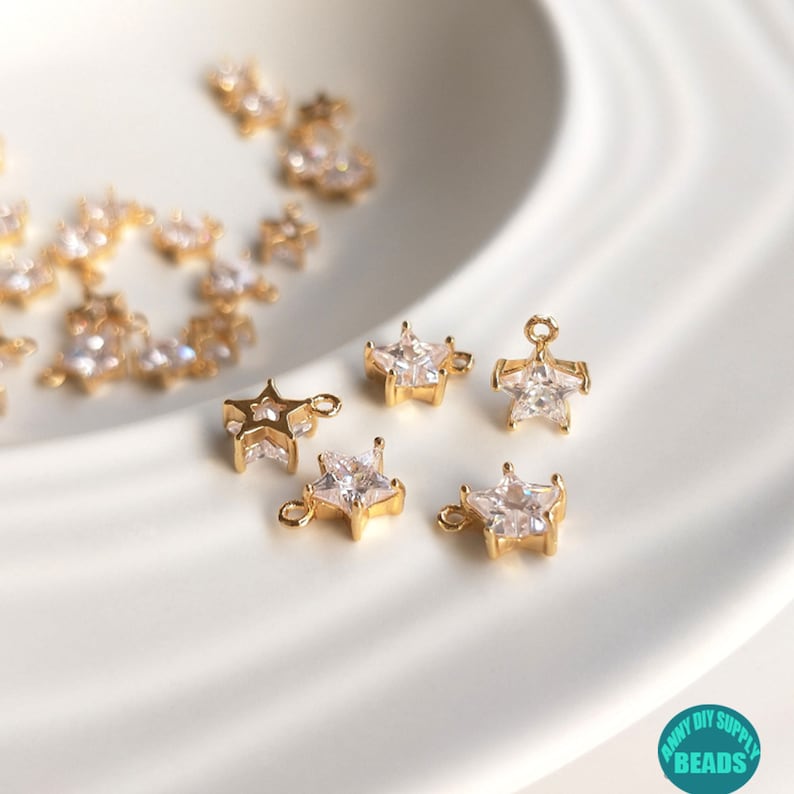 Puede incluir: Encantos dorados en forma de estrella con acentos de cristal transparente. Los encantos tienen un bucle para sujetar a joyas u otras artesan&iacute;as.