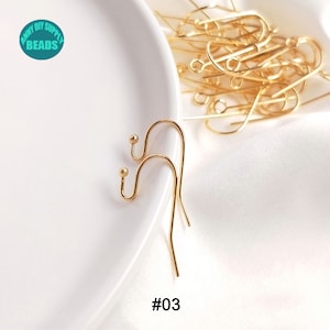 May include: Two gold-toned earring hooks with a small ball at the top of each hook. The hooks are on a white surface. #03