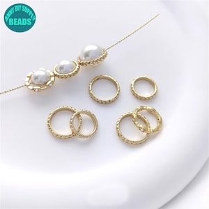 May include: A set of gold-toned metal rings and pearl beads. The rings have a textured design and some have a small clear rhinestone in the centre. The beads are white and have a textured design.