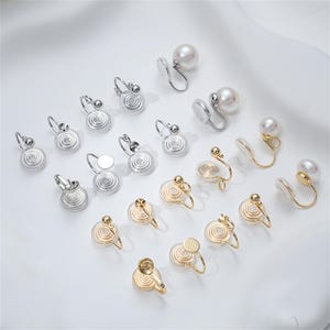 May include: An assortment of clip-on earrings in silver and gold tones, featuring pearl and spiral designs. The earrings are displayed on a white surface, showcasing various styles and sizes for accessorizing.