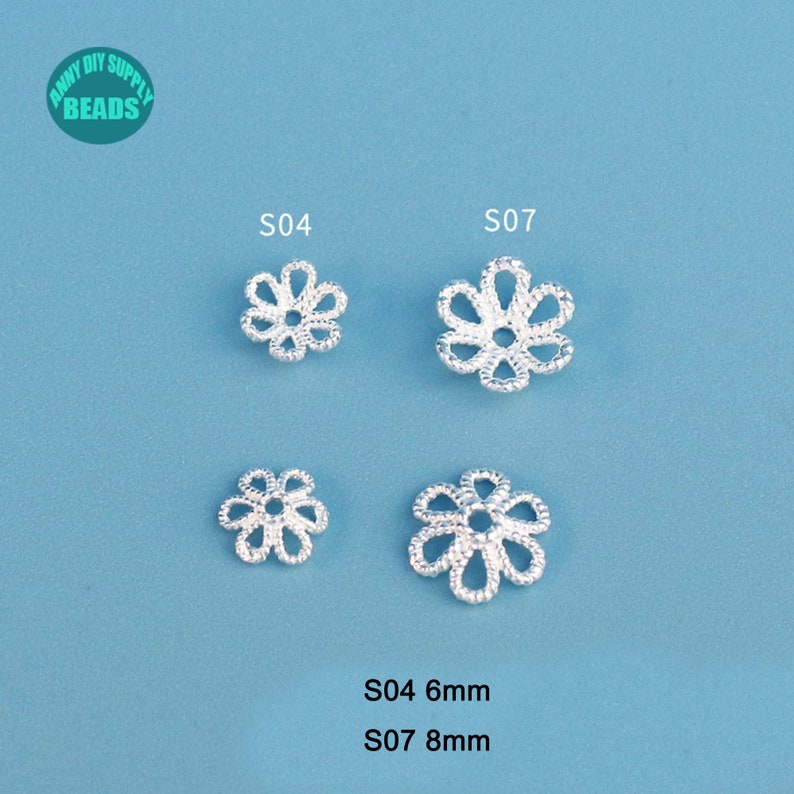 May include: Four silver-colored, flower-shaped beads. Two are labeled S04, measuring 6mm, and two are labeled S07, measuring 8mm. The beads have a delicate, openwork design. The background is a solid light blue.