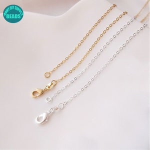 May include: Two chains, one gold and one silver, with lobster clasps. The chains are laid out on a white surface.