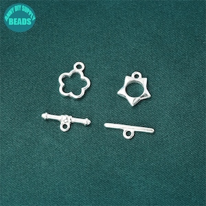 May include: Four silver-toned metal clasps for jewelry making. Two are toggle clasps, one is a star-shaped clasp, and one is a flower-shaped clasp.