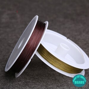 May include: Two spools of thin wire, one brown and one gold, are wound around white plastic spools. The spools are labeled "Anny DIY Supply Beads".