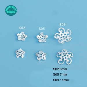 May include: Silver-colored flower-shaped beads in various designs and sizes. The beads are labeled S02 (6mm), S05 (7mm), and S09 (11mm). The image includes the text "Anny DIY Supply Beads" in a green circle.