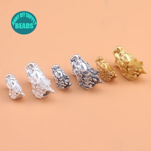 May include: Five silver and gold dragon head bead caps. The bead caps are in different sizes and are arranged in a row from smallest to largest. The bead caps are on a light brown surface.