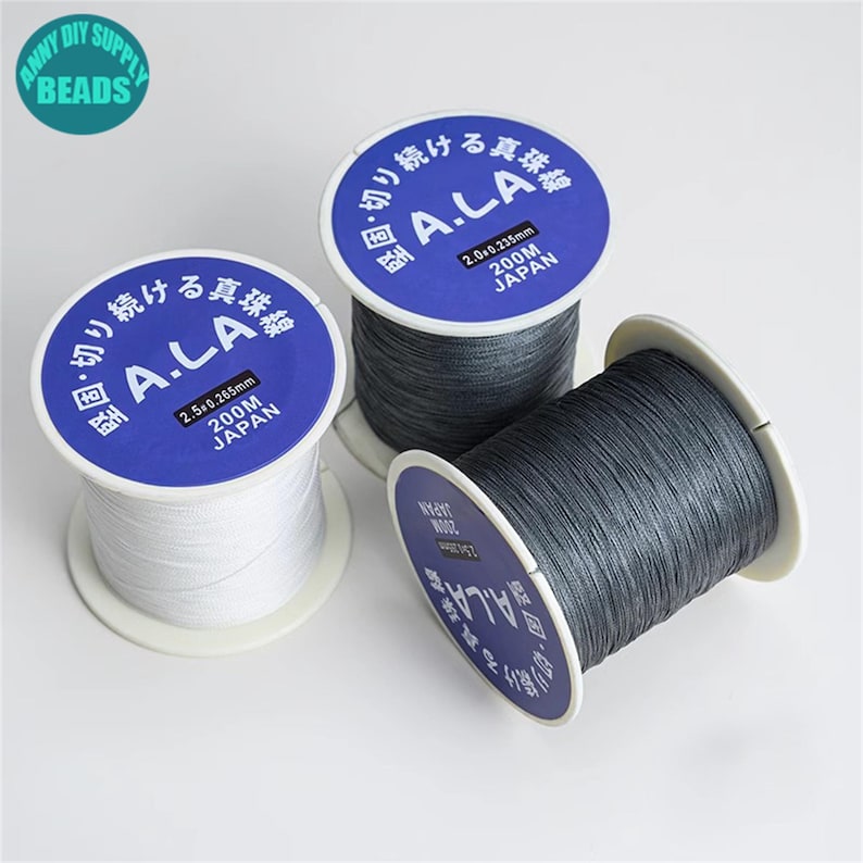 Puede incluir: Tres carretes de hilo de pesca gris y blanco. Los carretes est&aacute;n etiquetados "A.L.A.  2.5 x 0.265mm 200M JAP&Oacute;N" y "A.L.A. 2.0 x 0.235mm 200M JAP&Oacute;N".