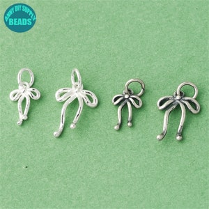 Op de afbeelding: Vier zilveren strikcharms met een lus aan de bovenkant om aan sieraden te bevestigen. De strikken hebben allemaal hetzelfde ontwerp, maar variëren in grootte.