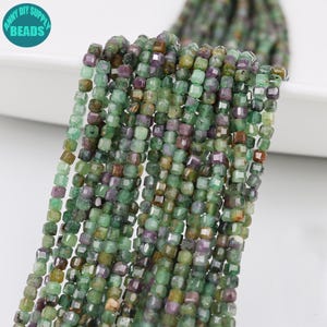 May include: Strands of square-cut beads in shades of green, purple, and brown. The beads are strung together, creating a textured and colorful display. The image includes a logo that says "ANNY DIY SUPPLY BEADS".