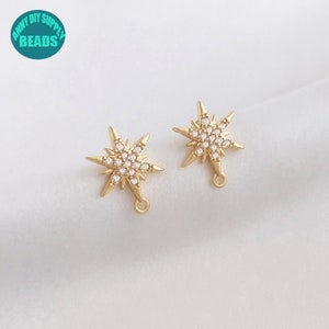 Op de afbeelding: Twee goudkleurige sterburst-bedels met heldere kristallen accenten en een springring. De bedels zijn op een witte achtergrond.